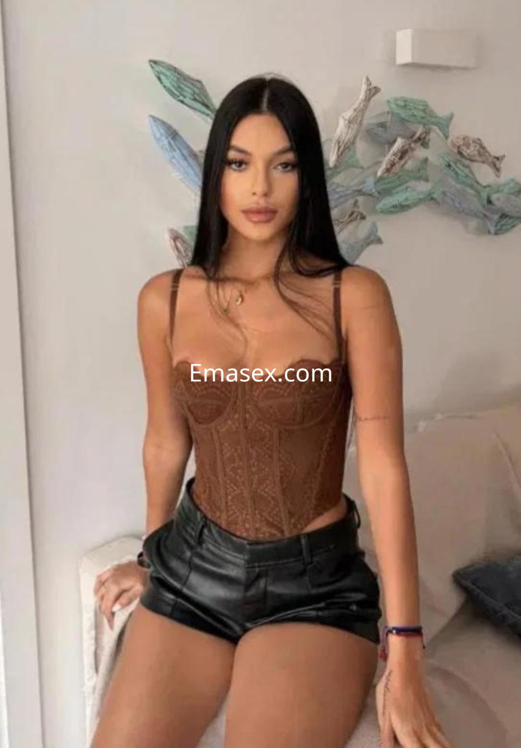 Puta en Badajoz luce un corset marrón y pantalones cortos de cuero negro, sentada en un ambiente elegante.