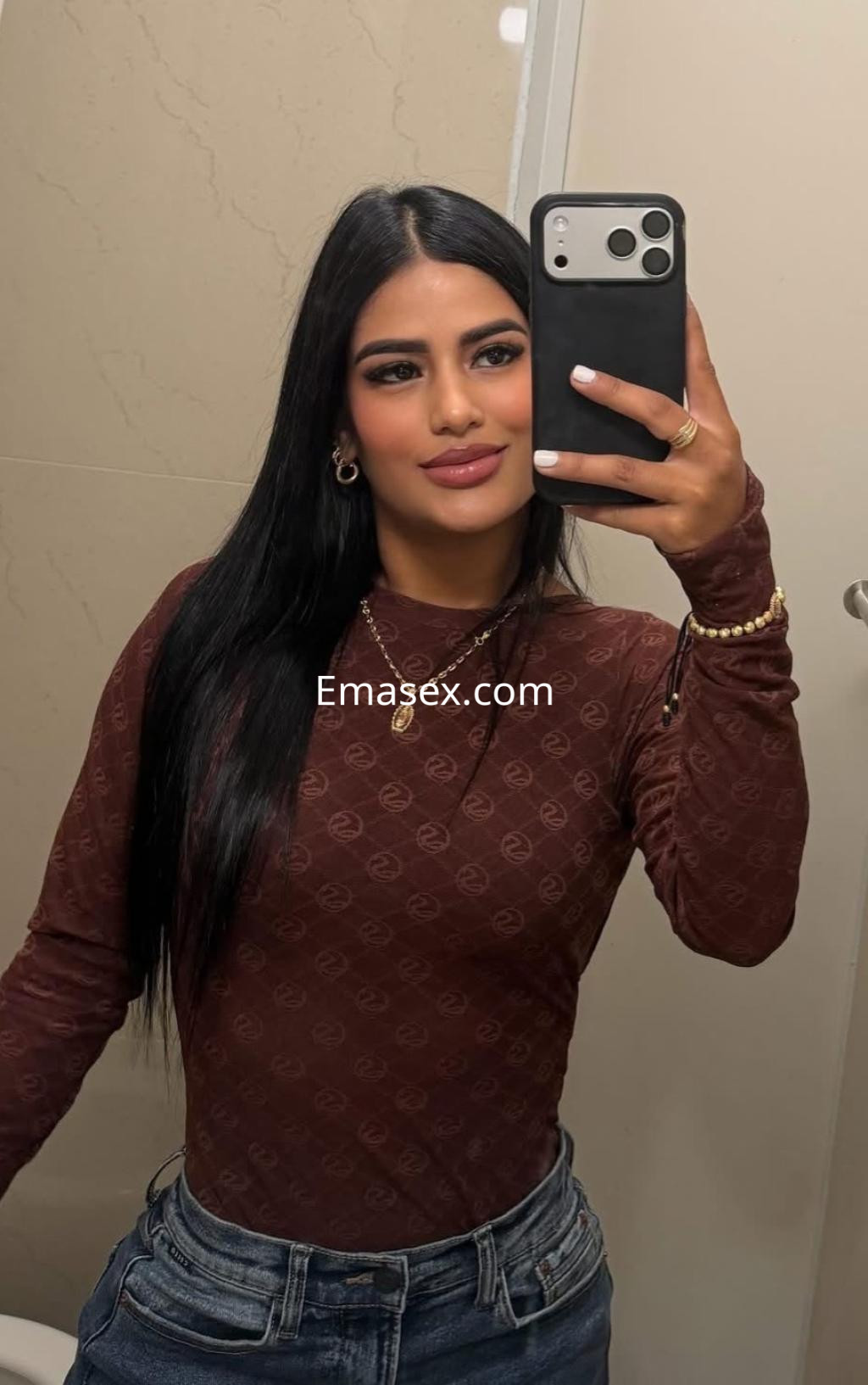 Escort en Bilbao posando en un baño con una blusa marrón ajustada y jeans, mostrando una expresión confiada.