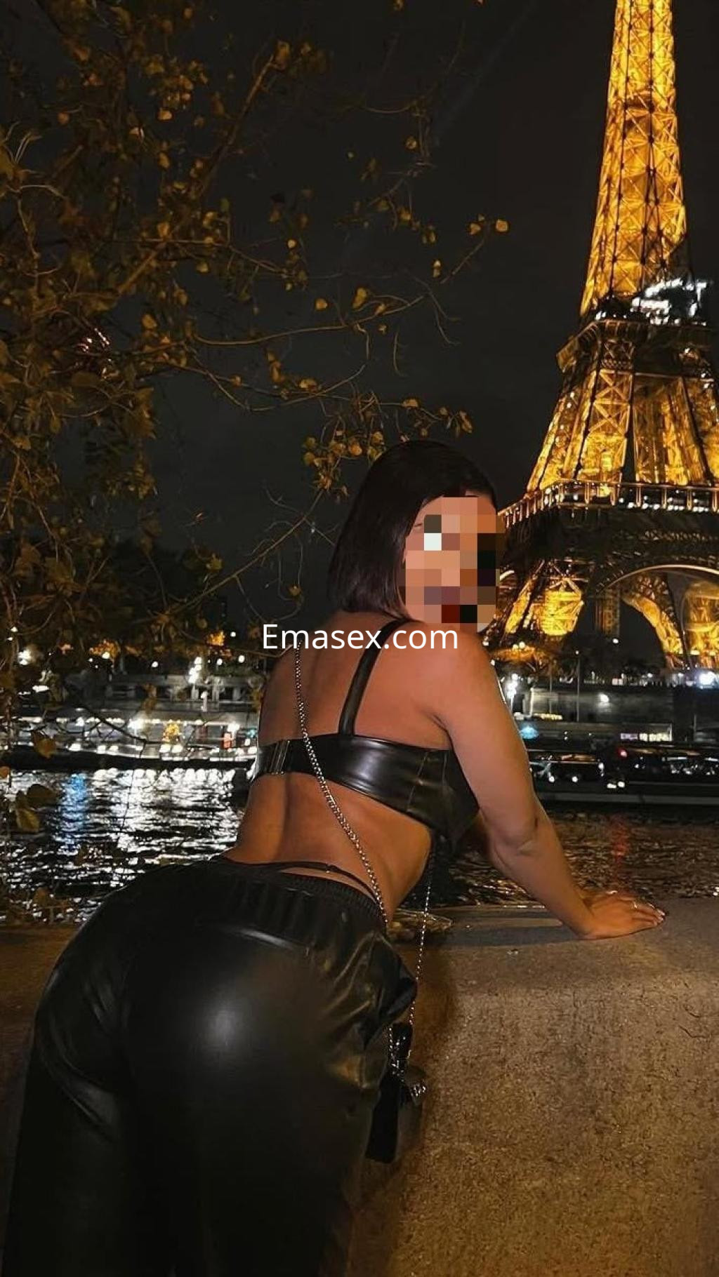 Puta en Badajoz posando de espaldas con ropa de cuero ajustada frente a la Torre Eiffel iluminada de noche.