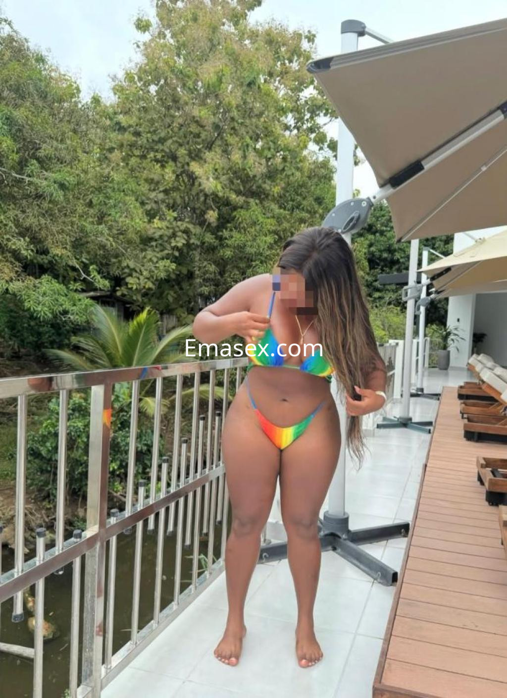 La puta se encuentra en una terraza en Girona, luciendo un bikini multicolor y ajustándose el cabello.