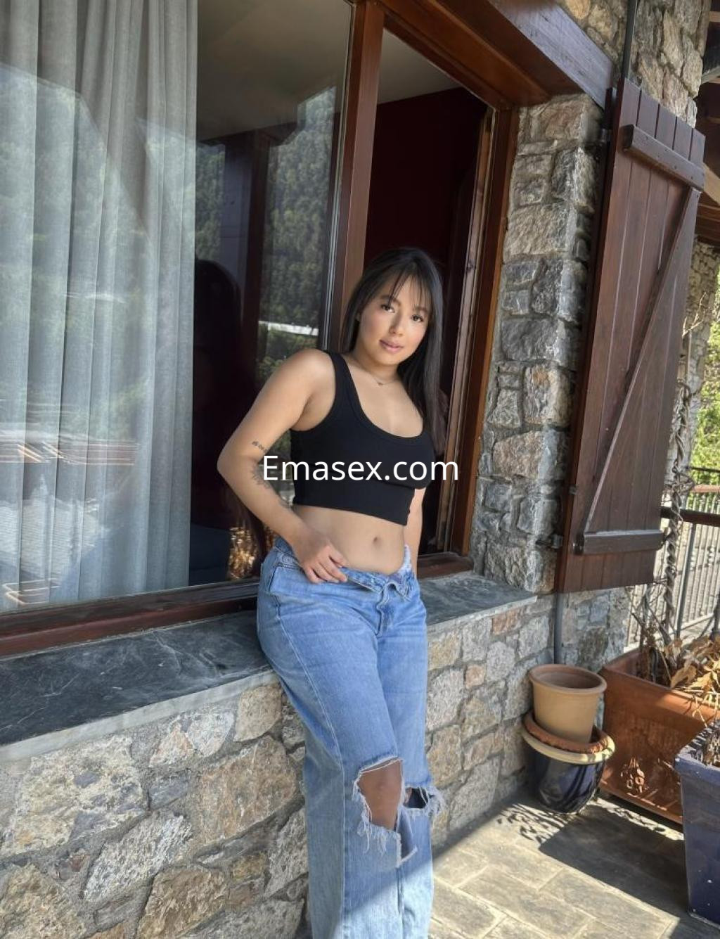 La puta está en Lleida, posando con un top negro y jeans rasgados, apoyada en una ventana de piedra.
