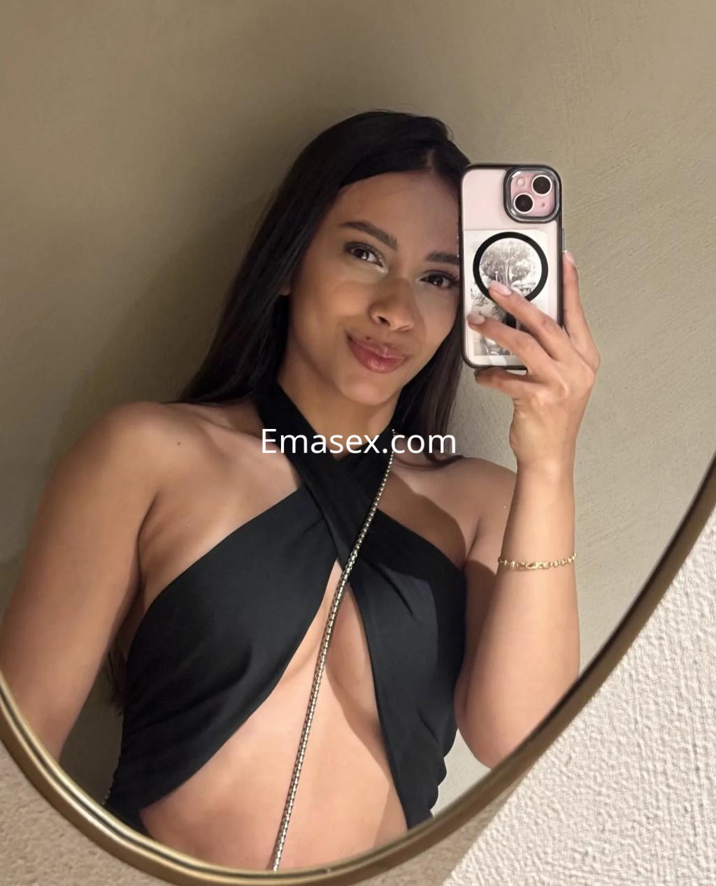 Escort en Málaga con cabello lacio y oscuro, posando frente a un espejo con un top negro que resalta su figura.