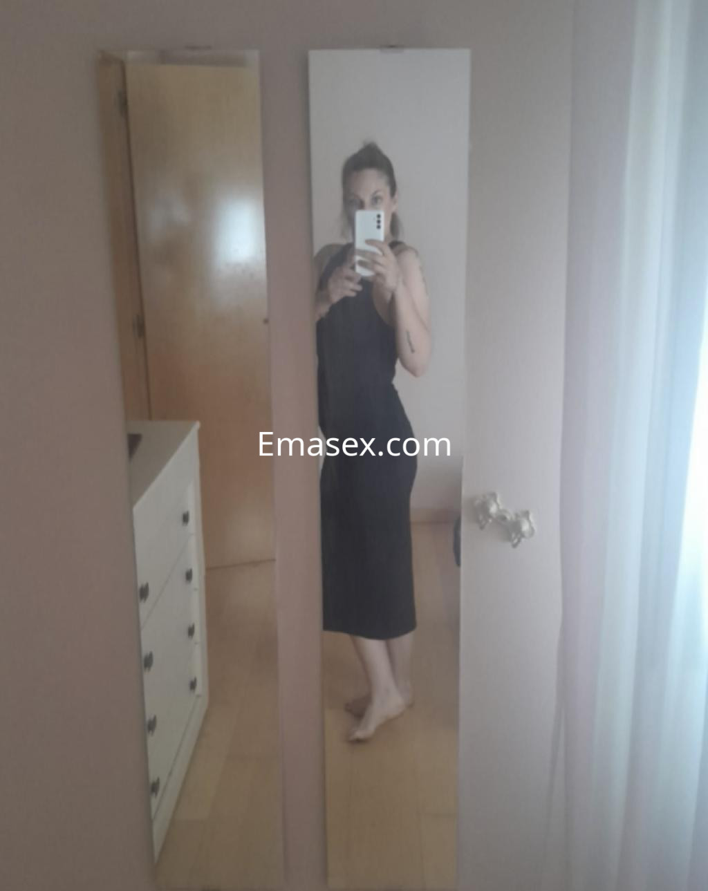 Escort en Salamanca tomando una selfie frente a un espejo, vistiendo un vestido negro y con el cabello recogido.