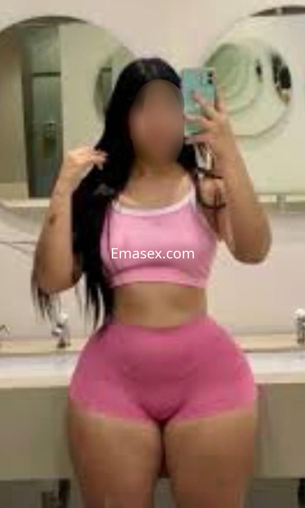Escort en Albacete con cabello largo y oscuro, viste un conjunto deportivo rosa mientras posa en un baño.