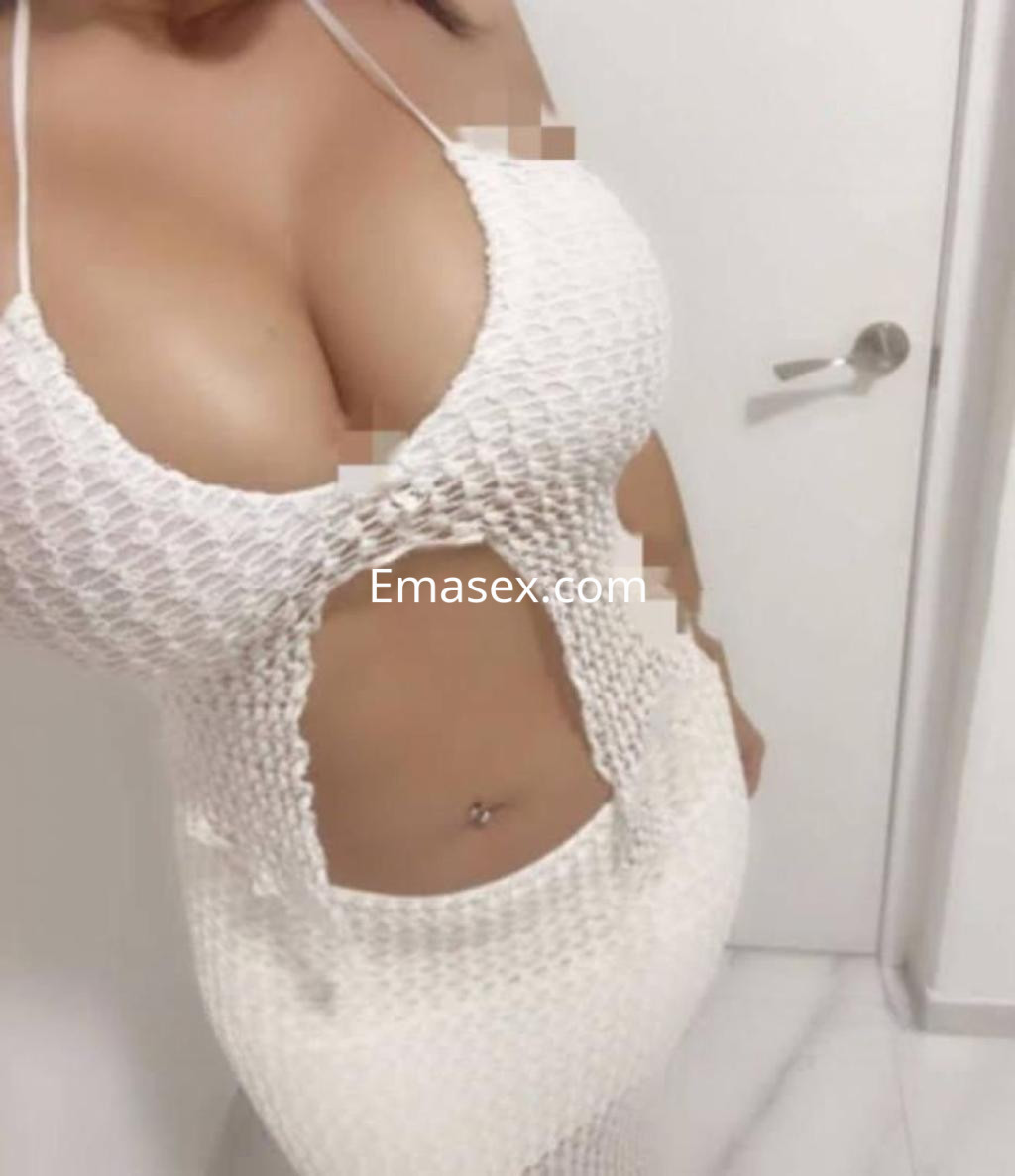 Escort en Almería con vestido blanco de diseño ajustado, destacando su figura y un ambiente minimalista.