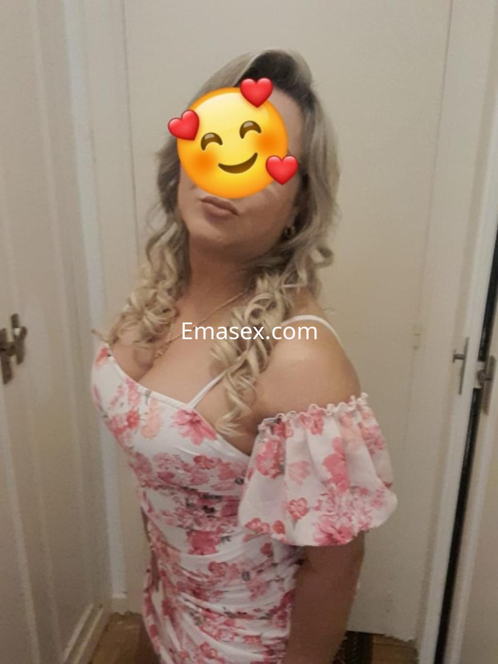 Puta con cabello rubio y rizado, viste un vestido de flores con mangas, en un ambiente interior de Burgos.