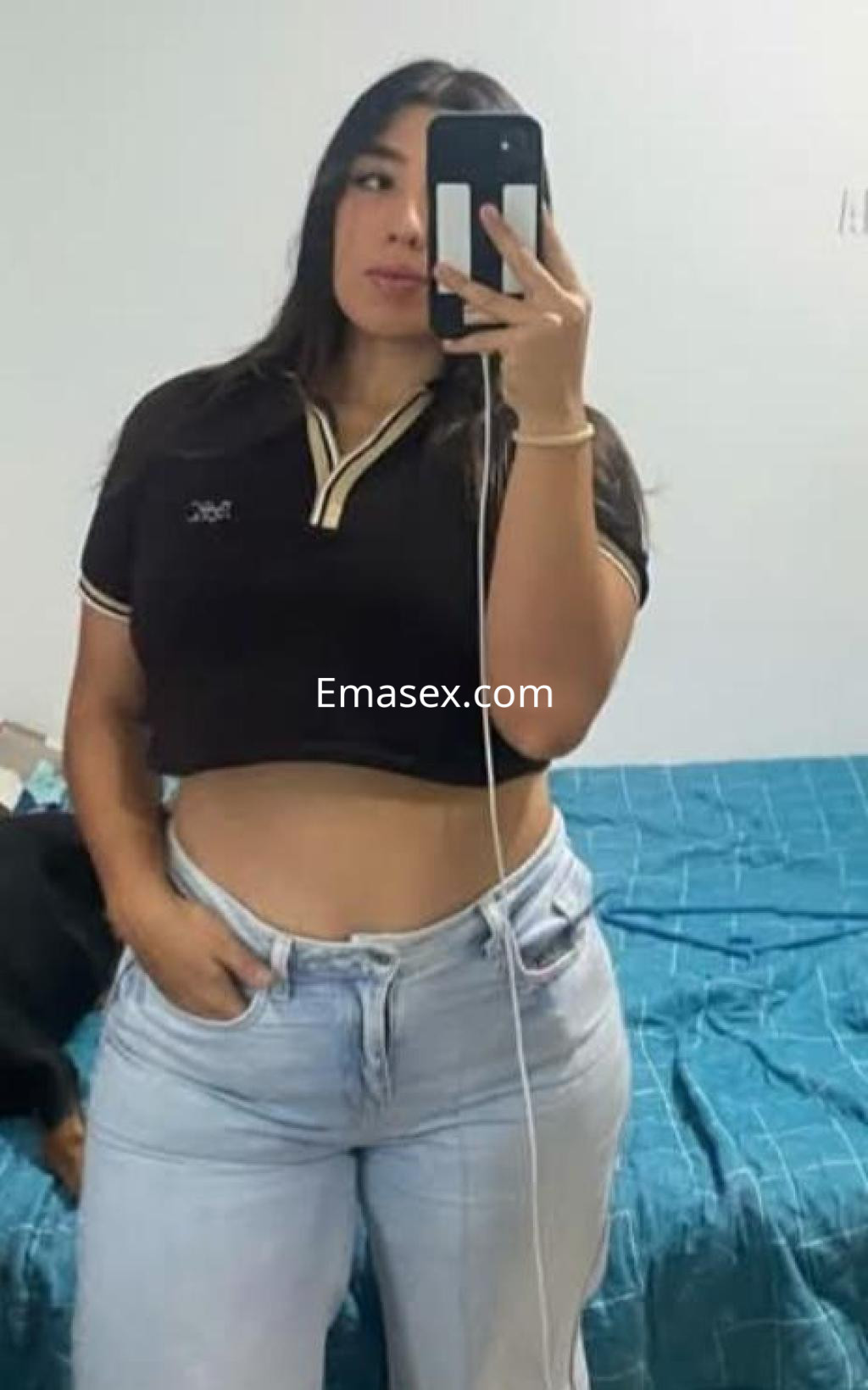 Escort en Granada con cabello largo y oscuro, viste una camiseta negra ajustada y jeans claros, posando con un espejo.