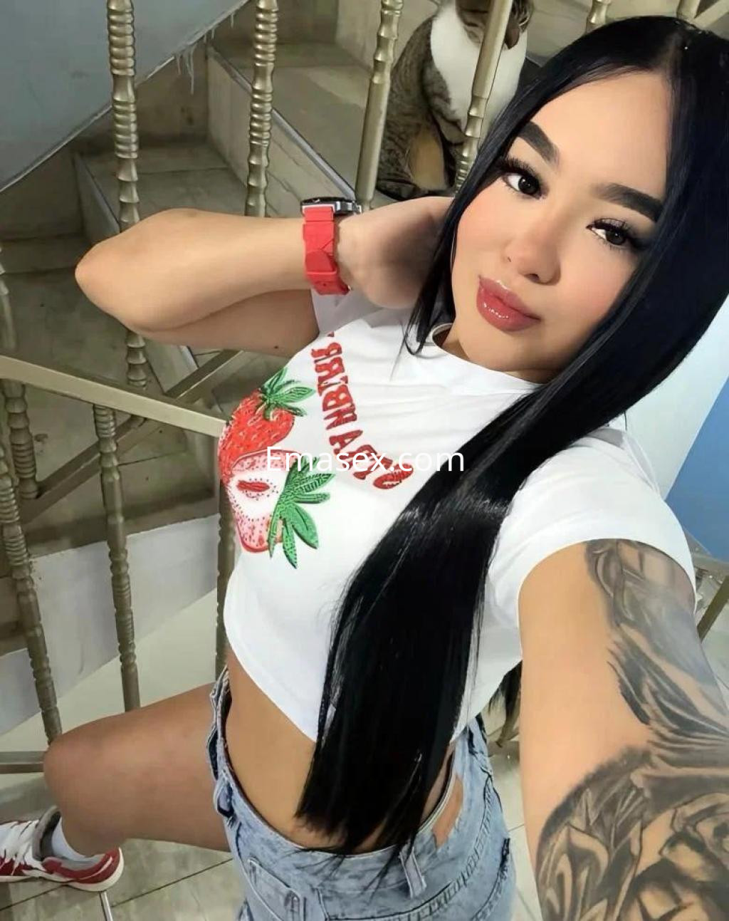 Puta con cabello largo y lacio, usando una camiseta corta blanca con estampado de fresa y shorts, en Huelva.