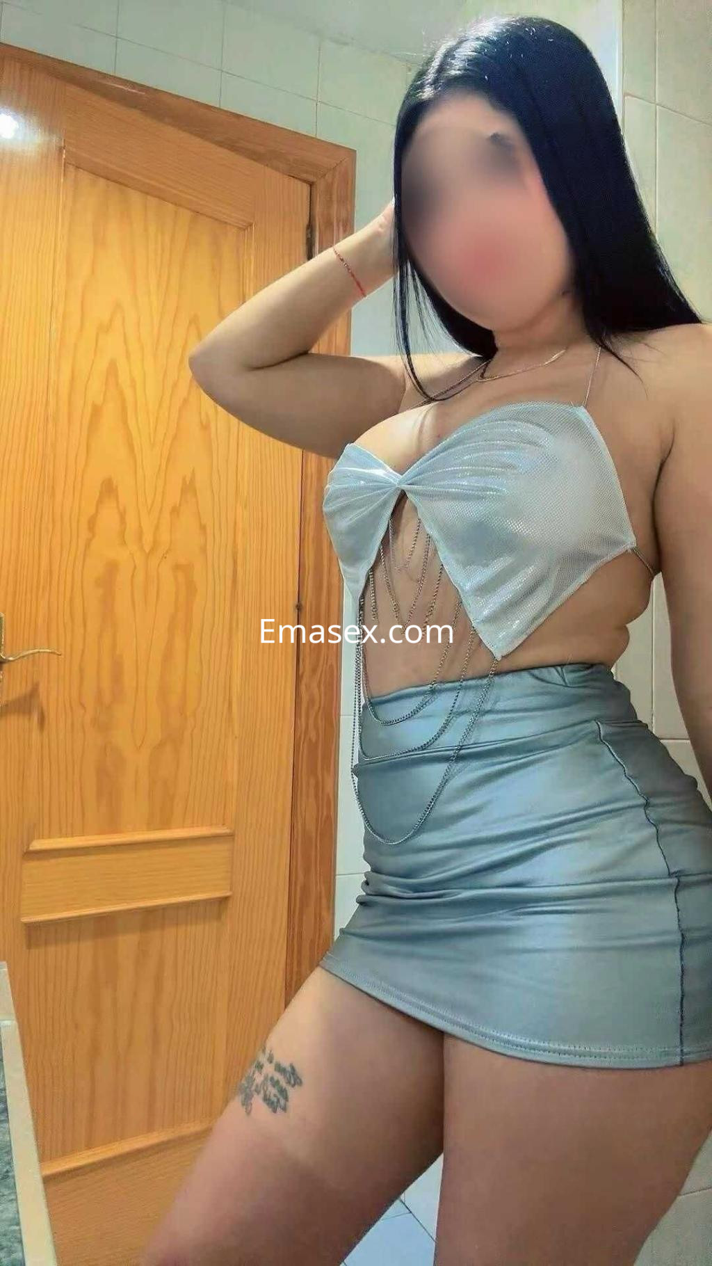 La puta en León lleva un top plateado con abertura y una falda ajustada, mostrando su figura en un ambiente interior.