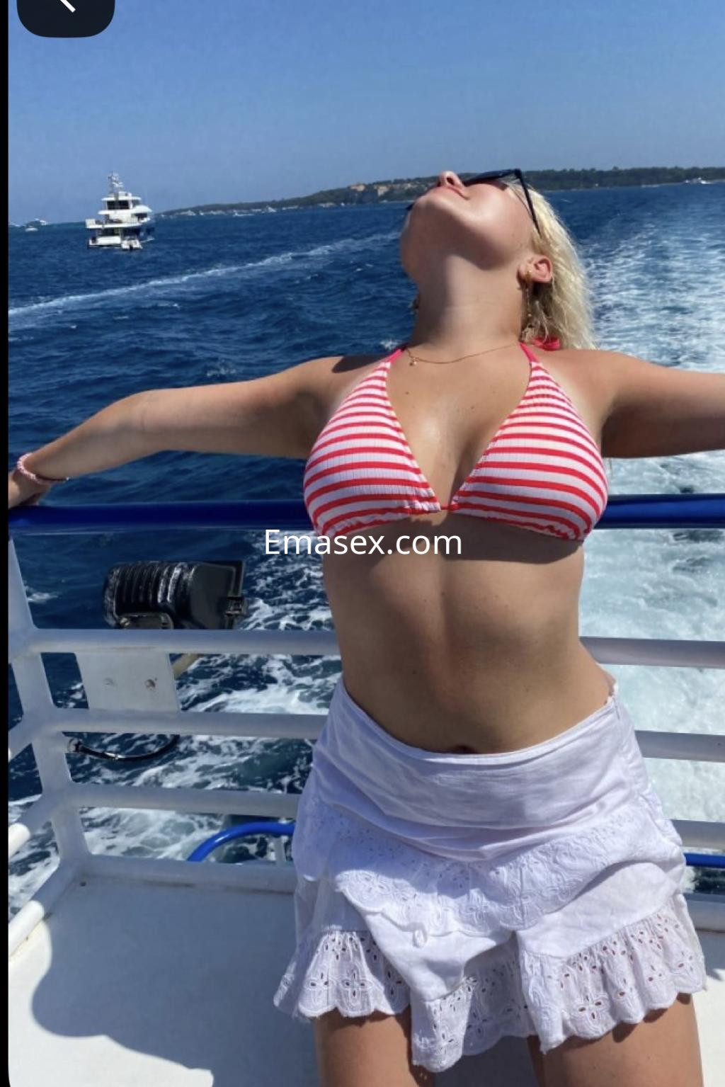 Escort en Madrid luciendo un bikini a rayas rojas y blancas, disfrutando del sol en un barco.