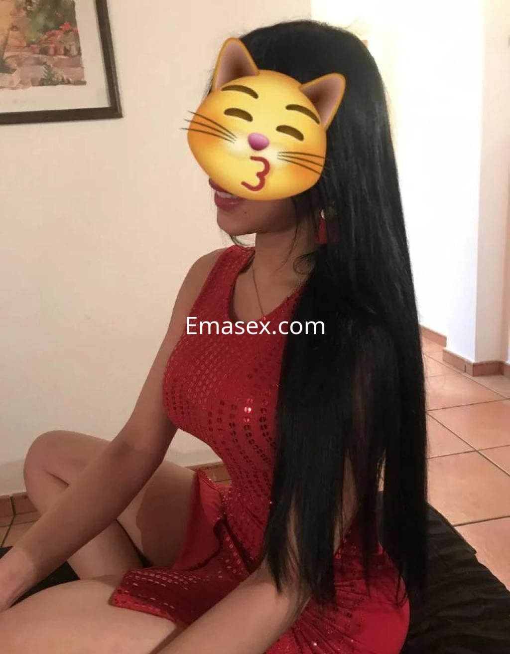 Escort en Alicante con cabello largo y negro, lleva un vestido rojo ajustado y está sentada en una cama.