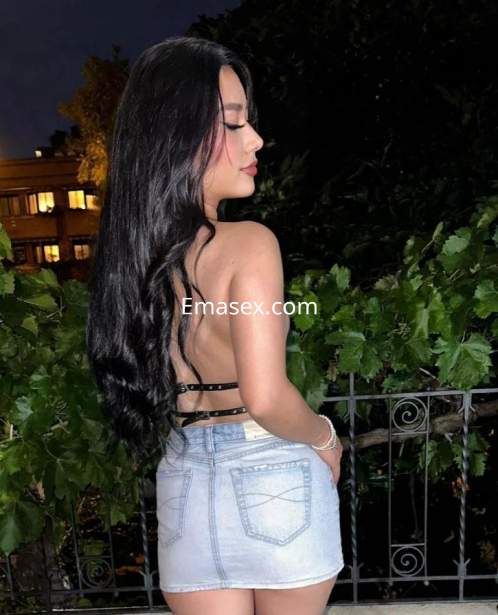 Escort de Alicante con cabello largo y oscuro, luciendo una blusa sin mangas y una falda corta, posando de perfil.
