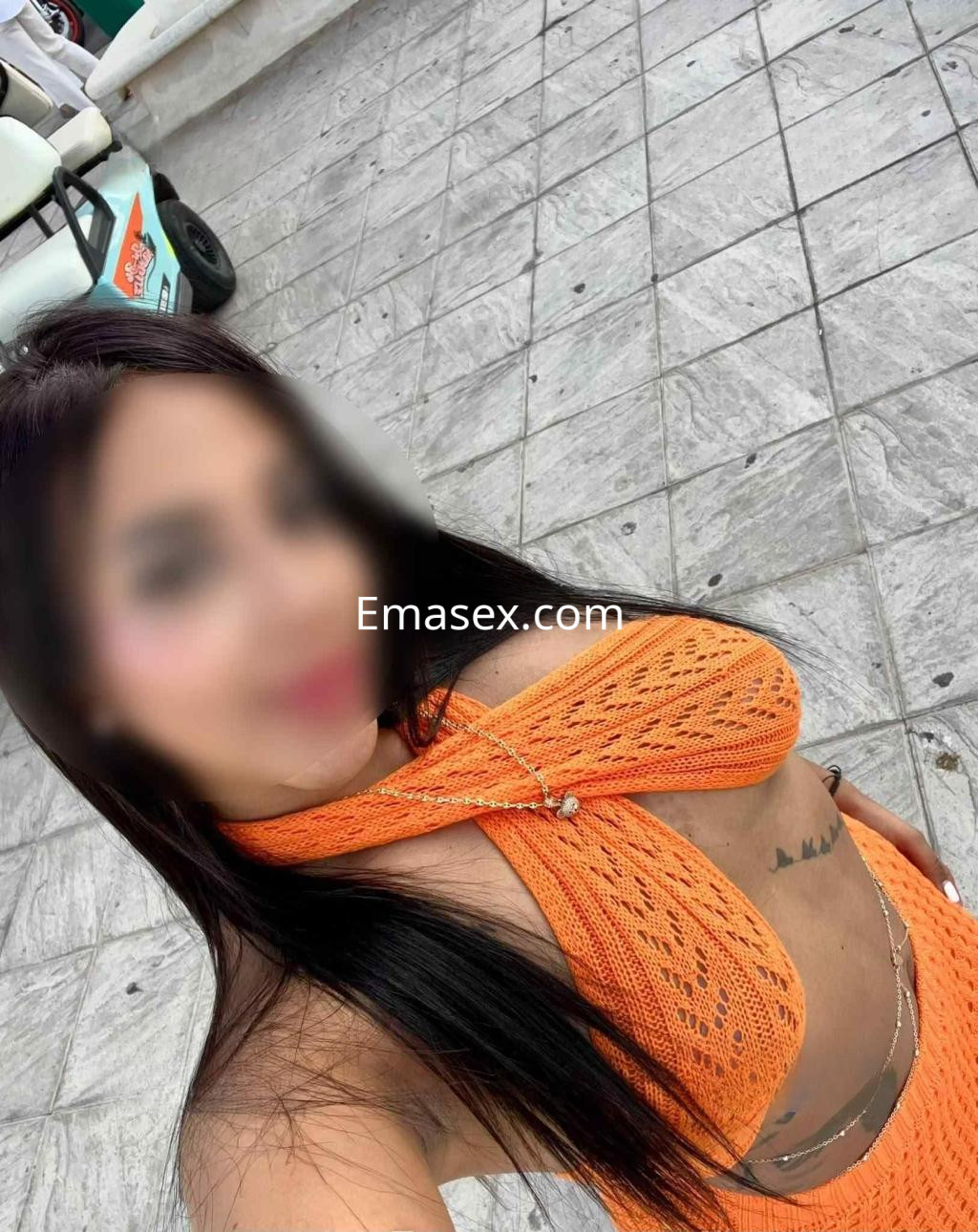 Puta con top de crochet naranja y falda a juego, posando en un entorno exterior de Almería.