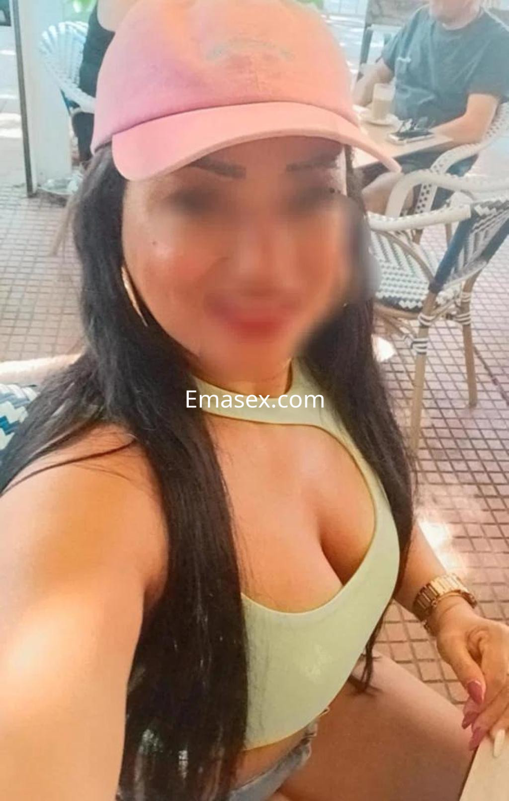 Escort en Almería con gorra rosa y top verde, posando con un fondo de terraza y un ambiente relajado.