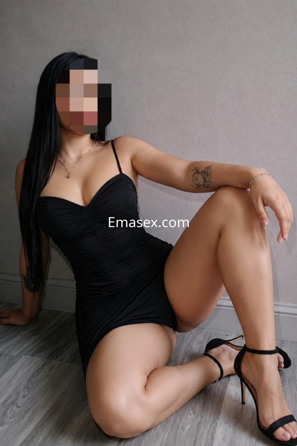 Escort en Castellón, posando de lado en un vestido negro ajustado, con tacones y cabello largo.