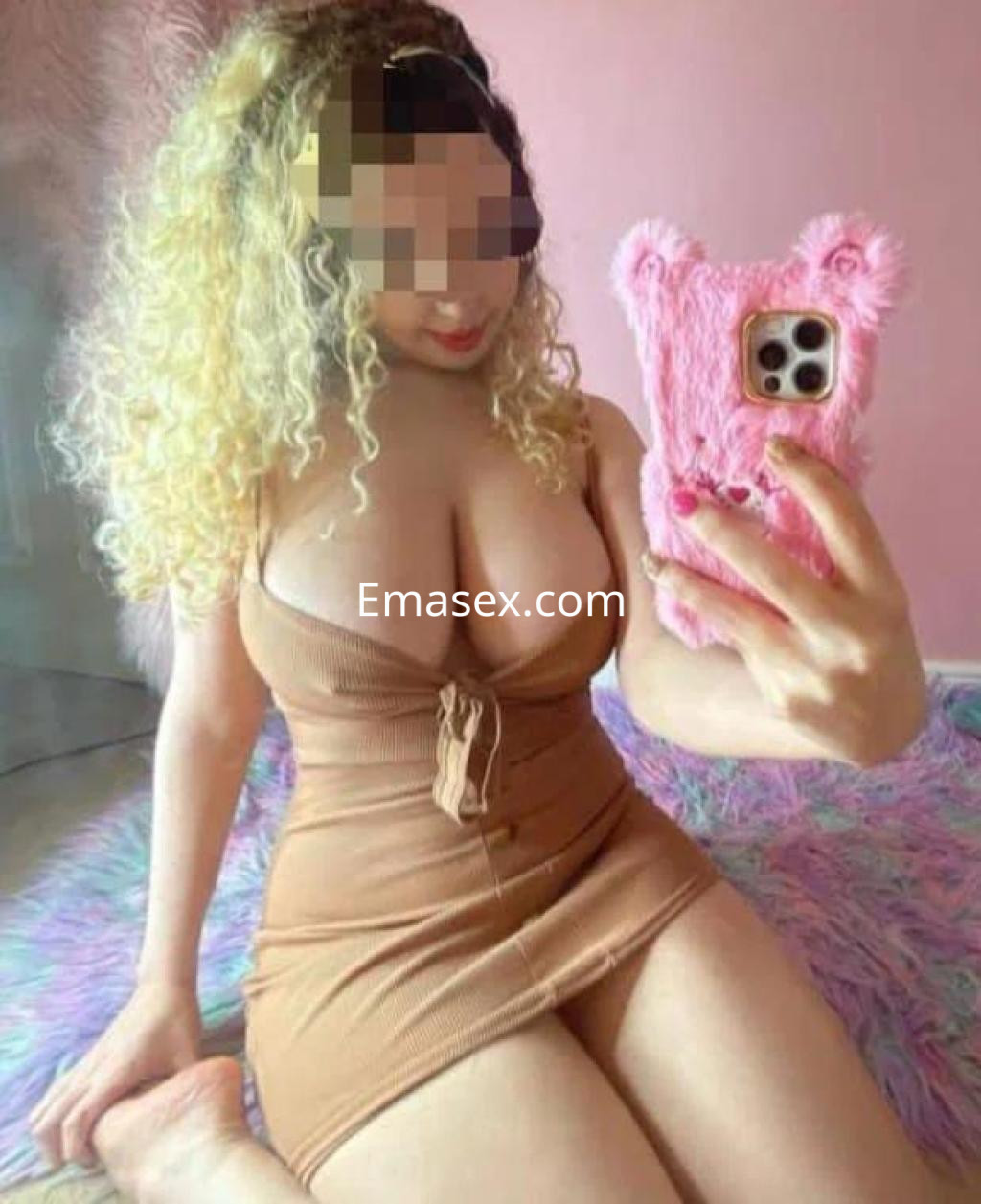 Escort en Pontevedra posando con un vestido ajustado de color marrón y sosteniendo un teléfono con funda rosa.