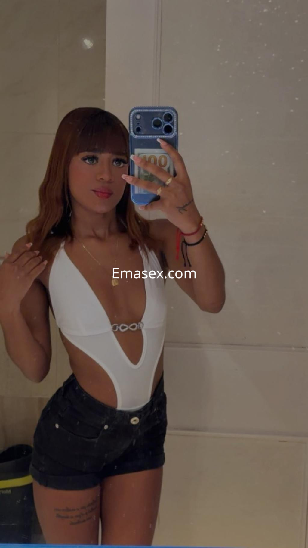 Escort en Tenerife con cabello castaño claro, luciendo un traje de baño blanco y shorts oscuros en un espejo.