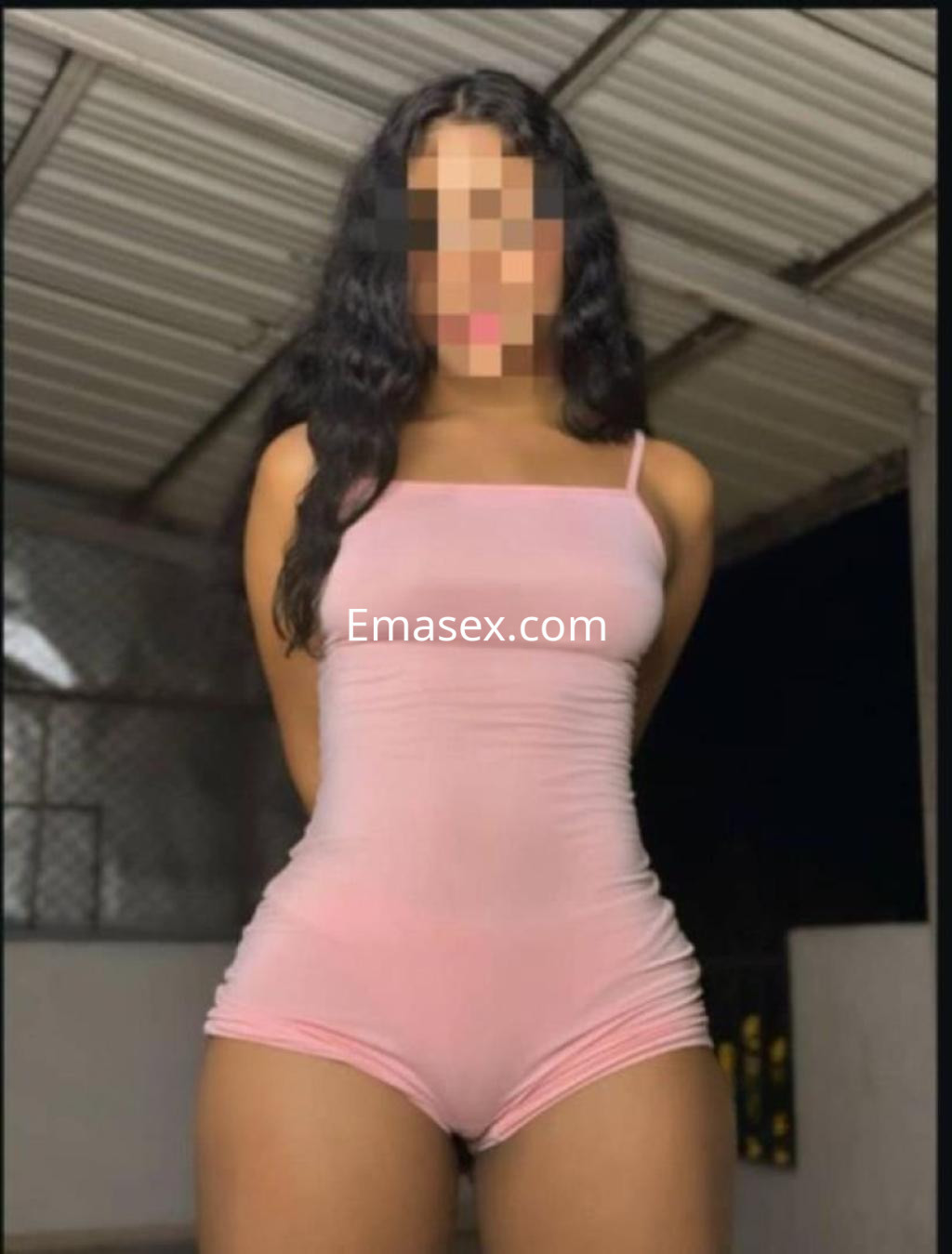 Puta en Sevilla luciendo un ajustado mono rosa que resalta su figura, con cabello largo y ondulado.