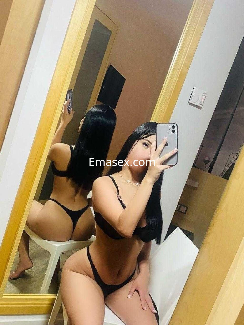 Escort en Sevilla posando en lencería negra frente a un espejo, con cabello largo y lacio.