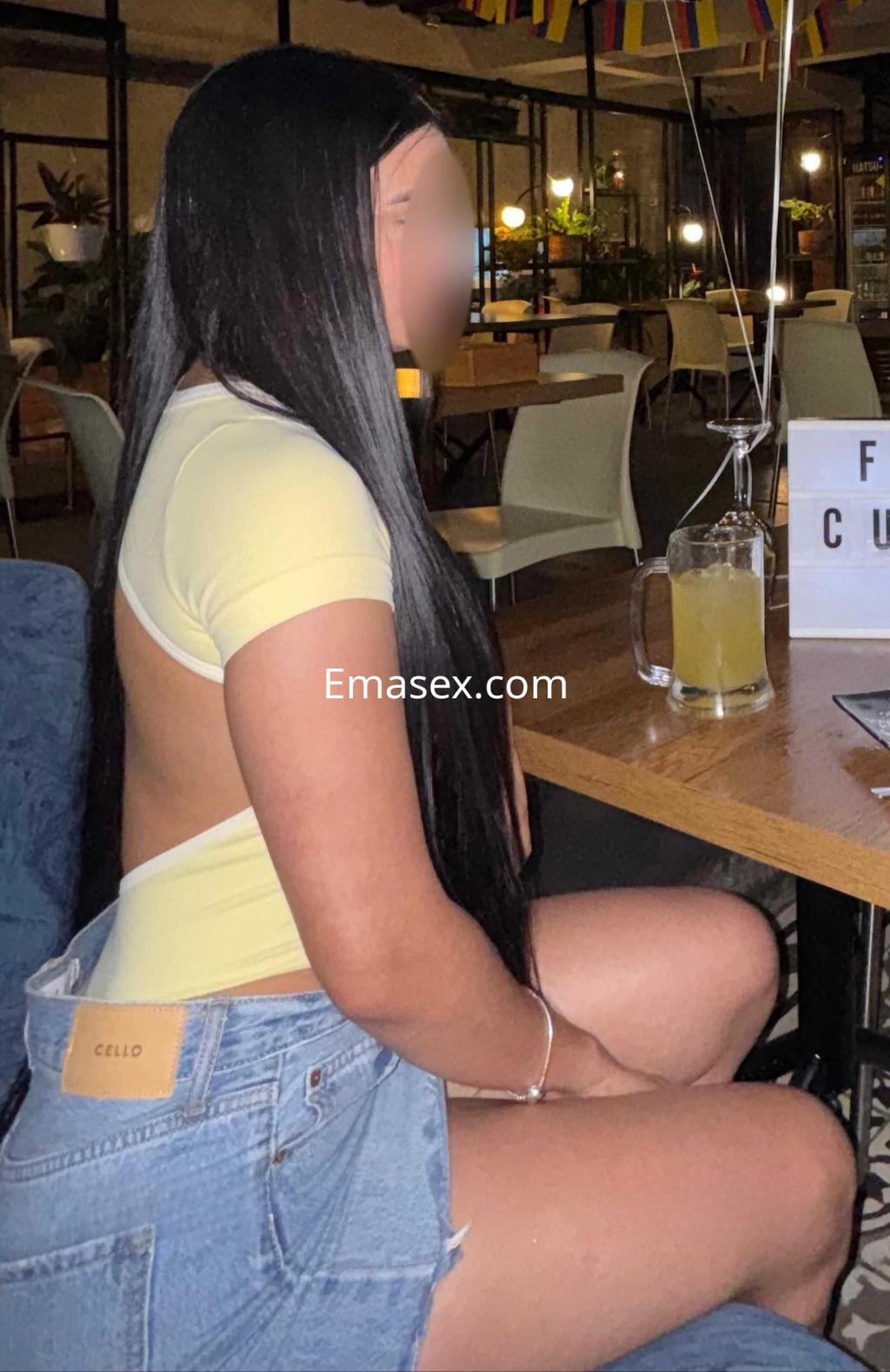 Puta de cabello largo y lacio, viste una blusa amarilla y shorts de mezclilla, sentada en un bar en Tarragona.