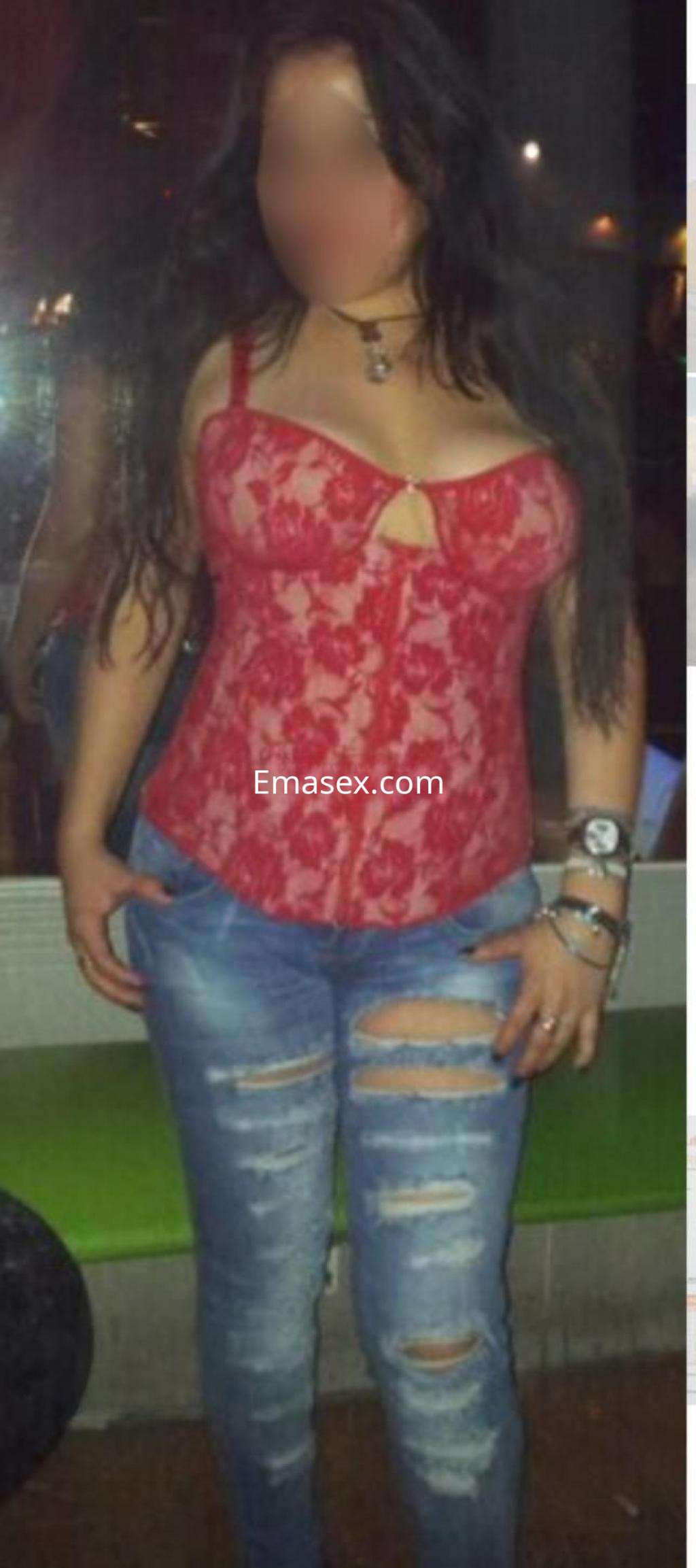 Puta en Toledo viste un corset rojo de encaje y jeans rasgados, mostrando su figura con cabello largo y oscuro.