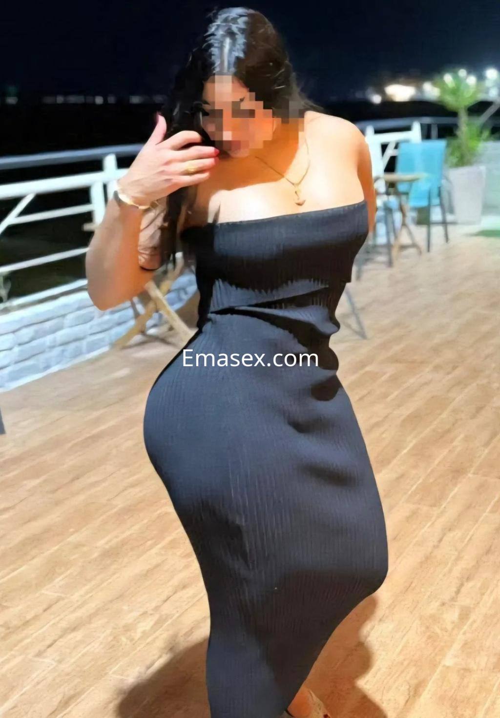 La puta luce un vestido negro ajustado, posando en un entorno al aire libre en Gijón, con una iluminación nocturna.