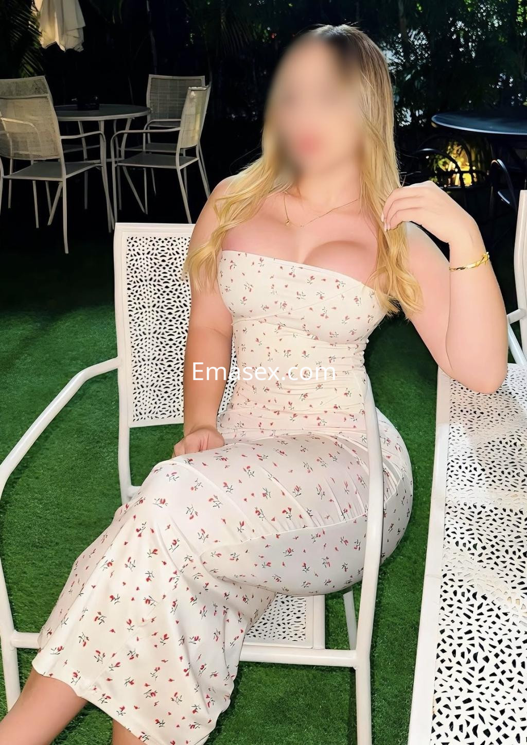 Escort en Oviedo sentada en una silla blanca, luciendo un vestido sin mangas de flores en un entorno verde.