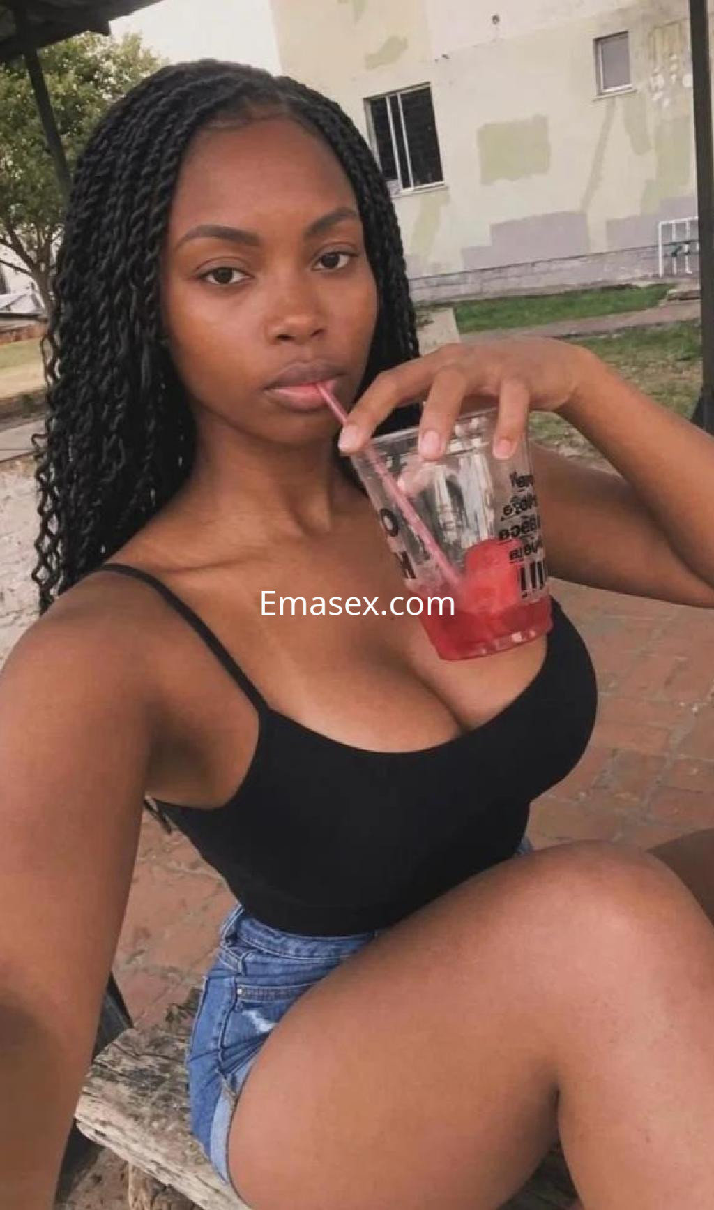 Escort en Coruña con cabello trenzado, blusa negra y pantalones cortos, sosteniendo un vaso con bebida.