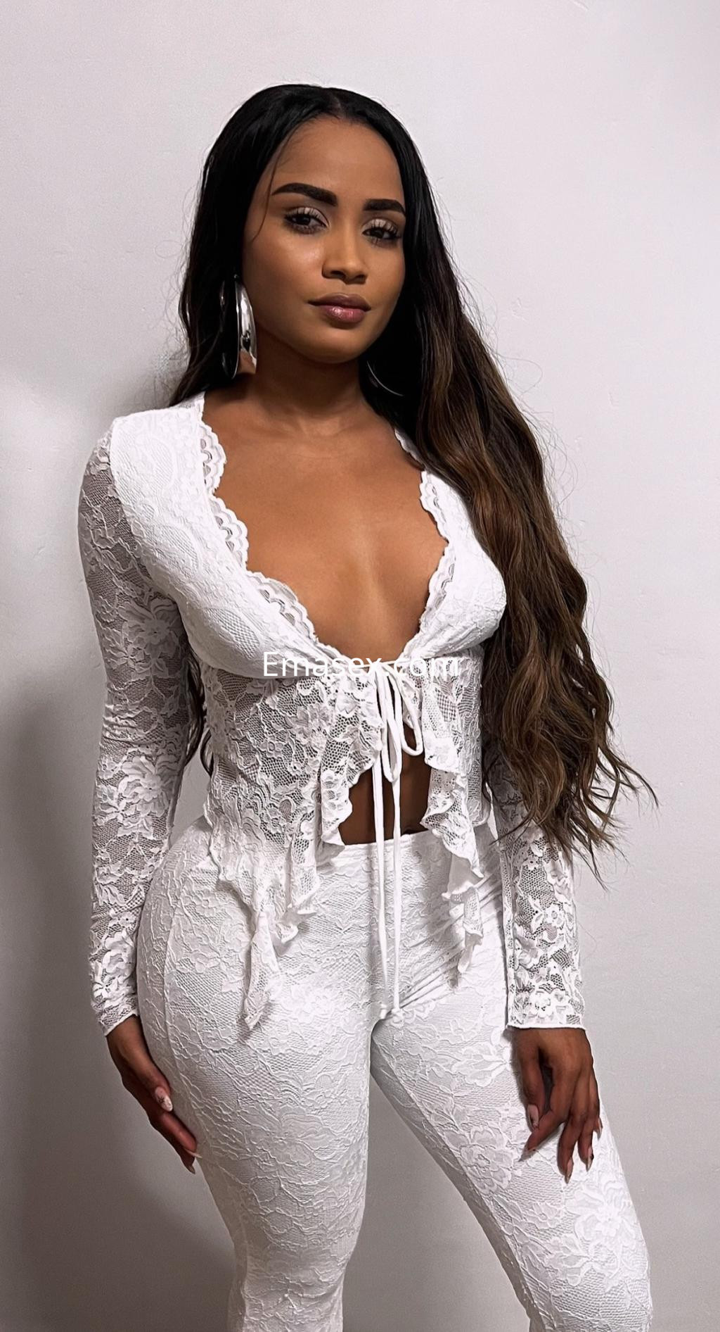 Escort en Vigo luciendo un conjunto de lencería blanca con encaje, cabello largo y ondulado, en un fondo neutro.