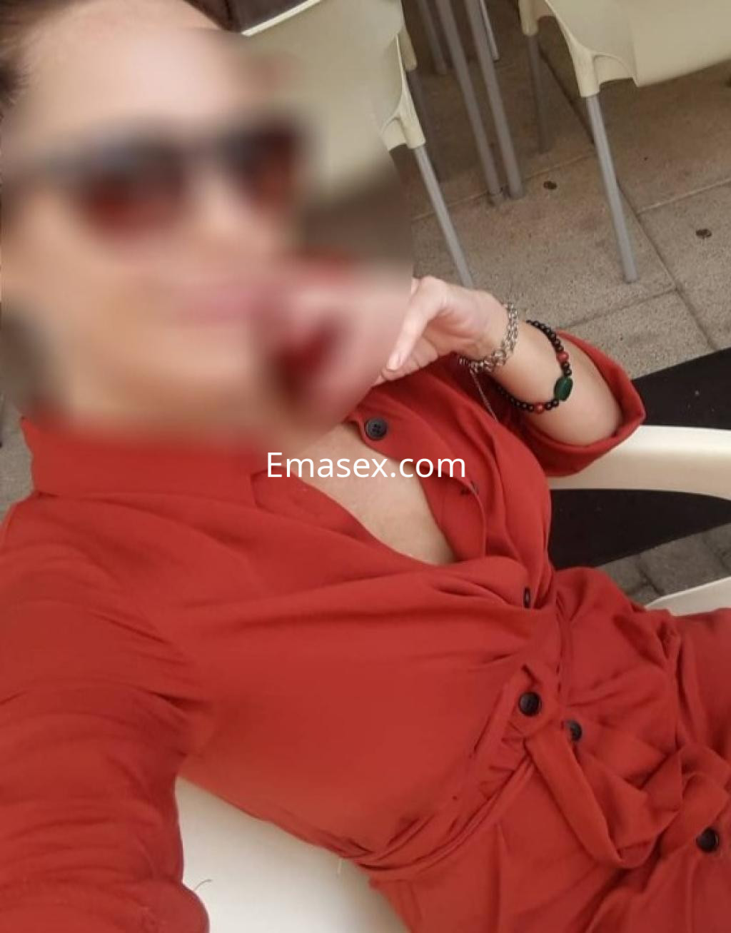 Puta en Burgos, posando con un vestido rojo, sentada en una silla y usando gafas de sol.