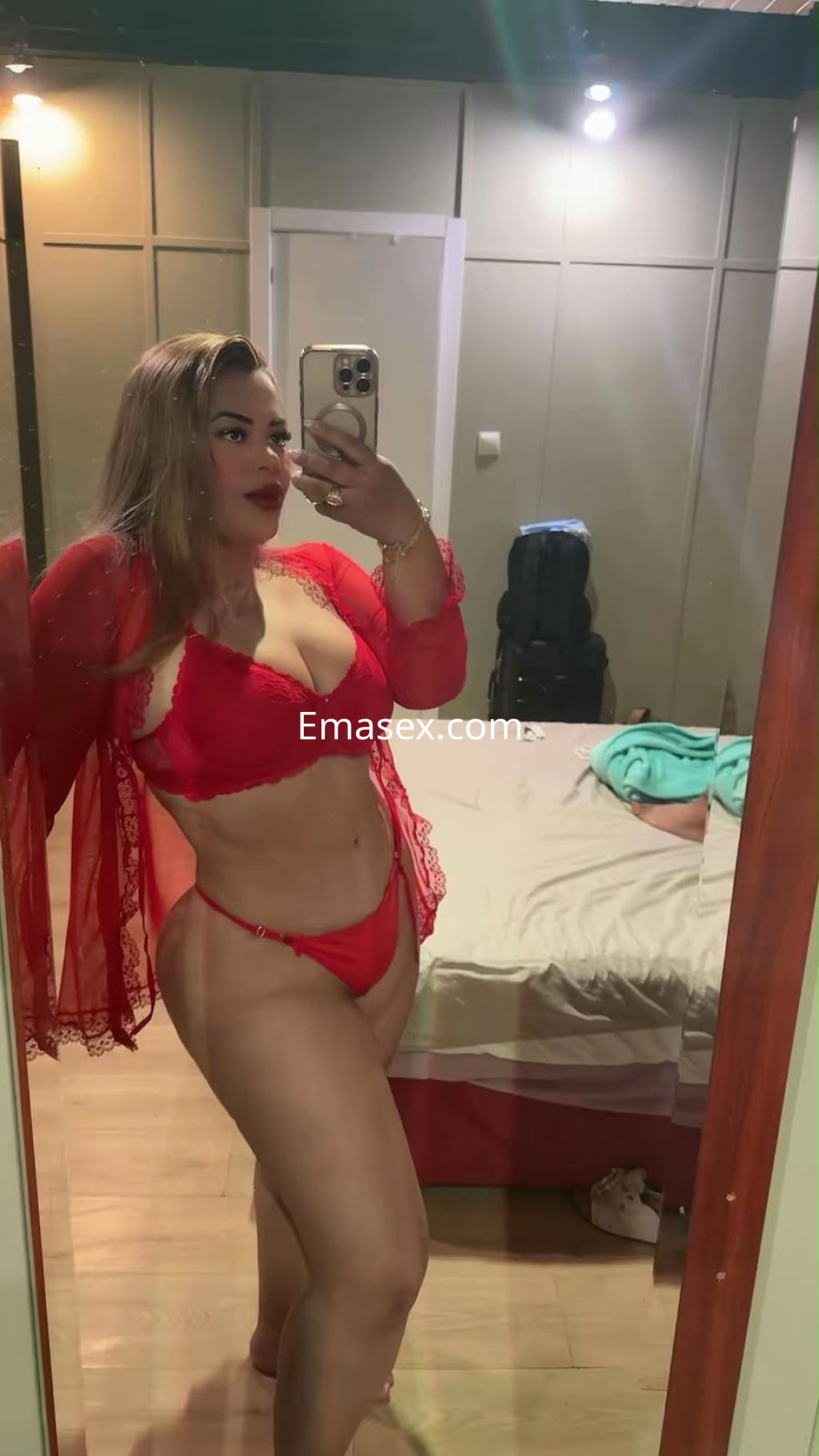 Escort en Bilbao luciendo un conjunto de lencería roja con un kimono semitransparente, posando frente a un espejo.