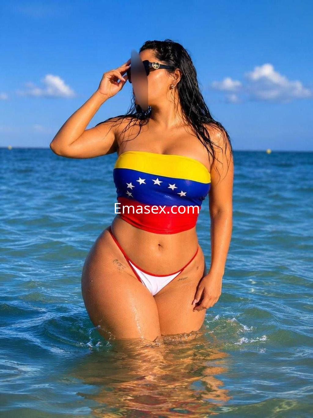 Escort en Albacete luciendo un bikini con los colores de la bandera venezolana, de pie en el agua.