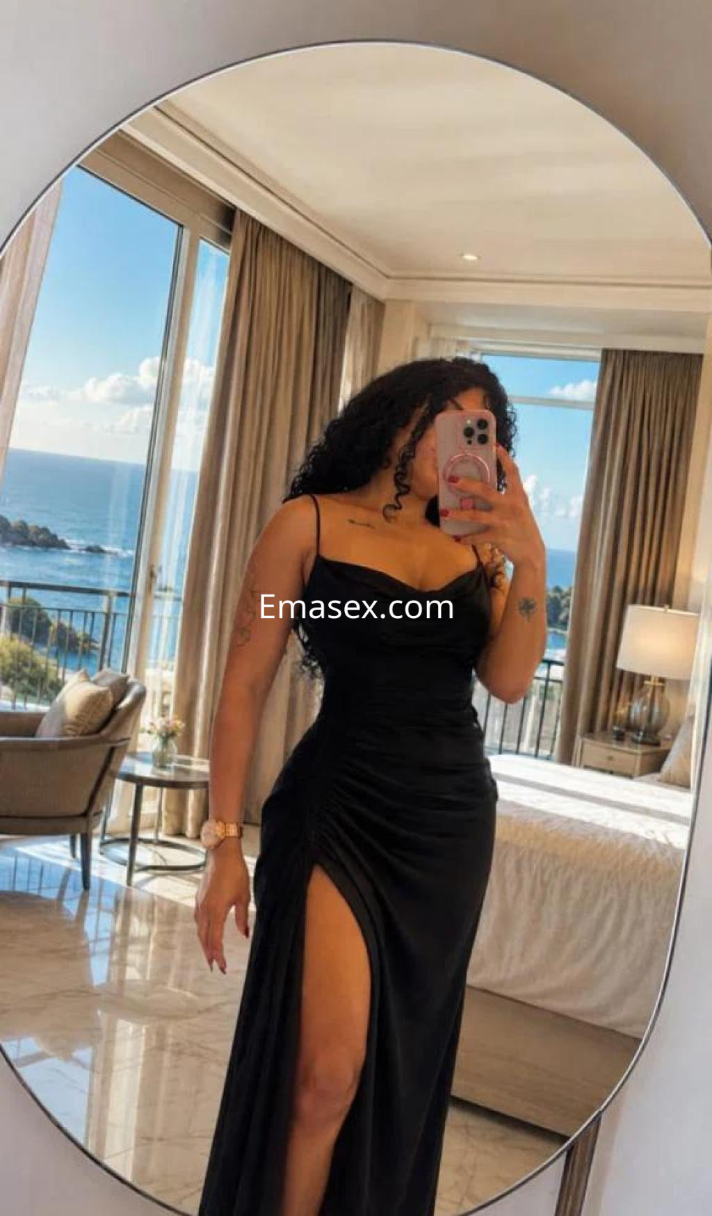 Escort en Badajoz con cabello rizado, luciendo un elegante vestido negro con abertura, en un entorno luminoso y moderno.