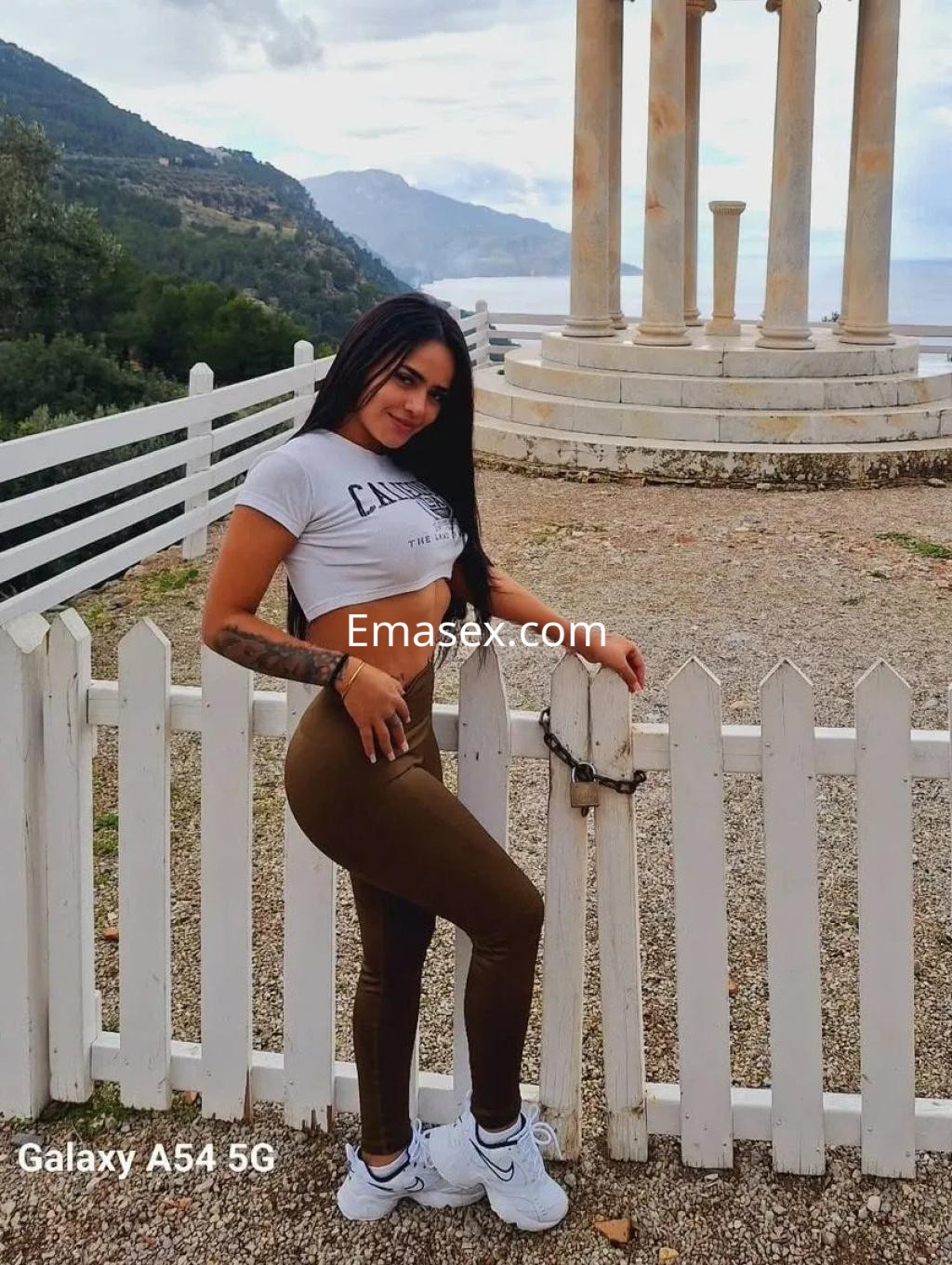 Escort en Palma de Mallorca posando frente a un paisaje montañoso, vestida con top corto gris y mallas marrones.