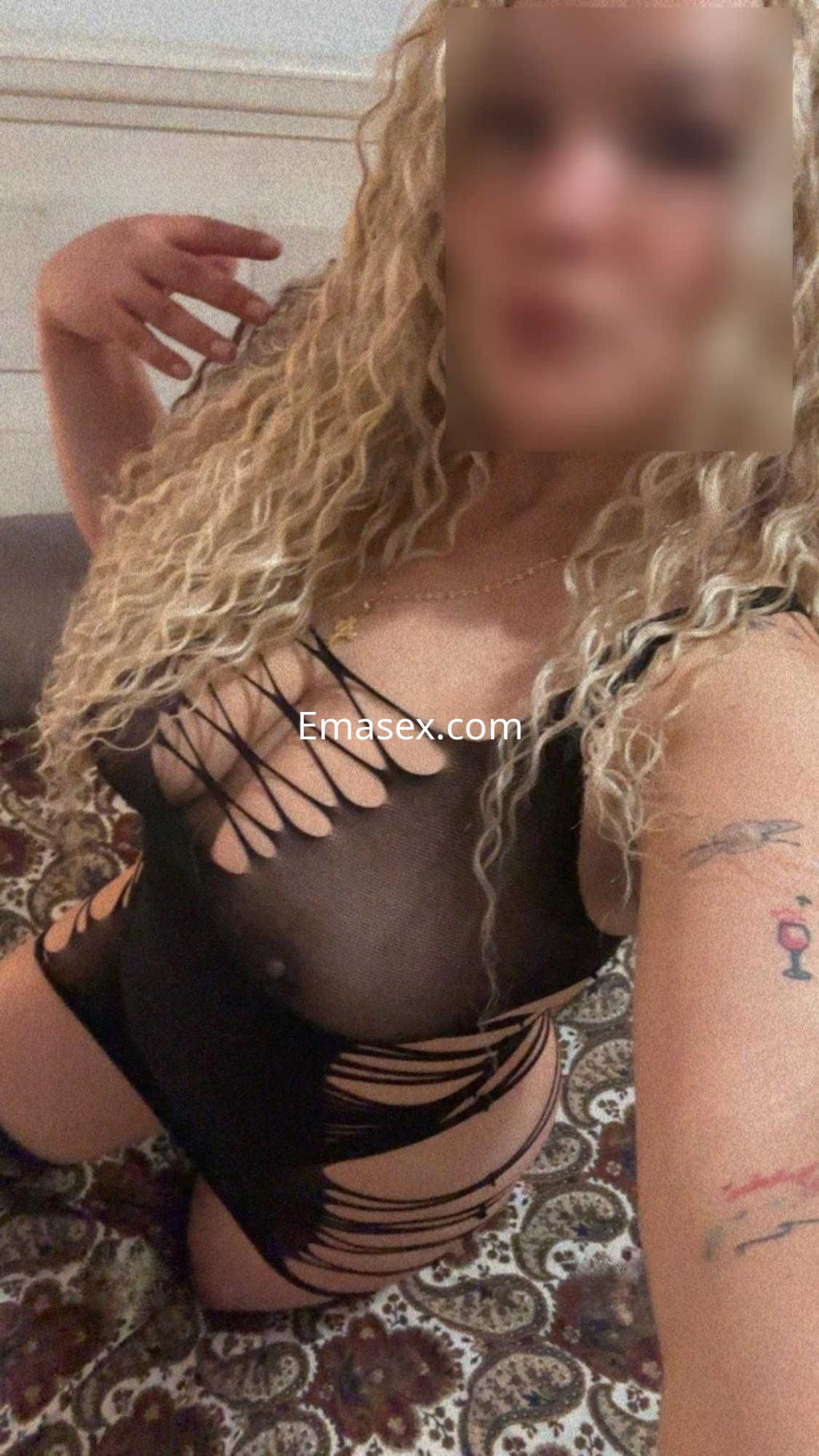 Escort en Huelva posando en lencería negra con detalles transparentes y cabello rizado, en un ambiente acogedor.