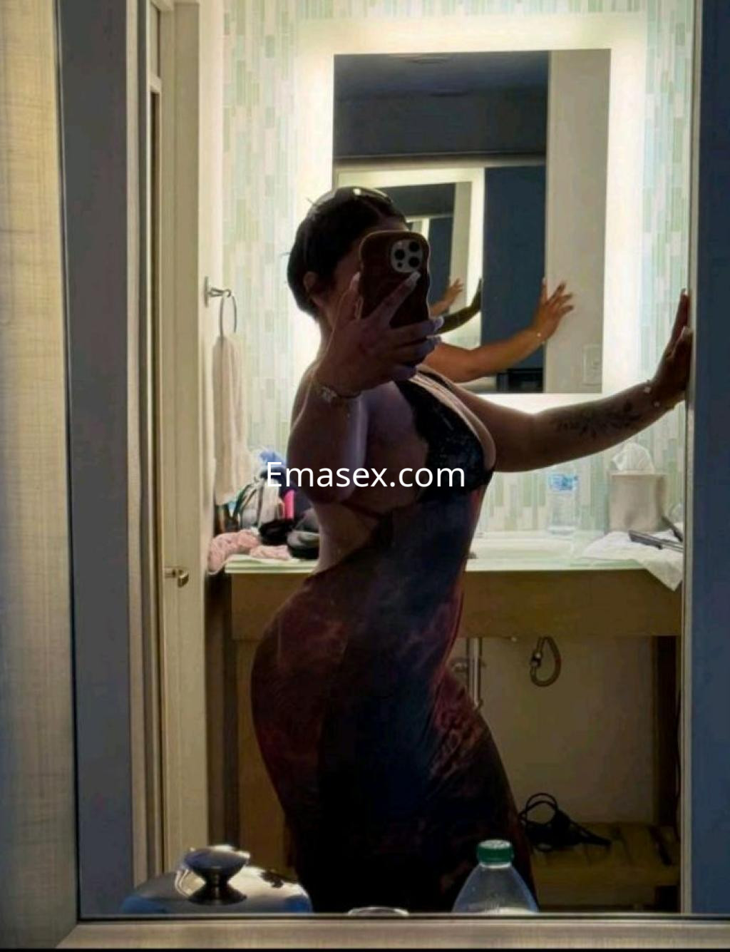 Escort en León, posando frente al espejo con un vestido ajustado y un fondo de baño moderno.