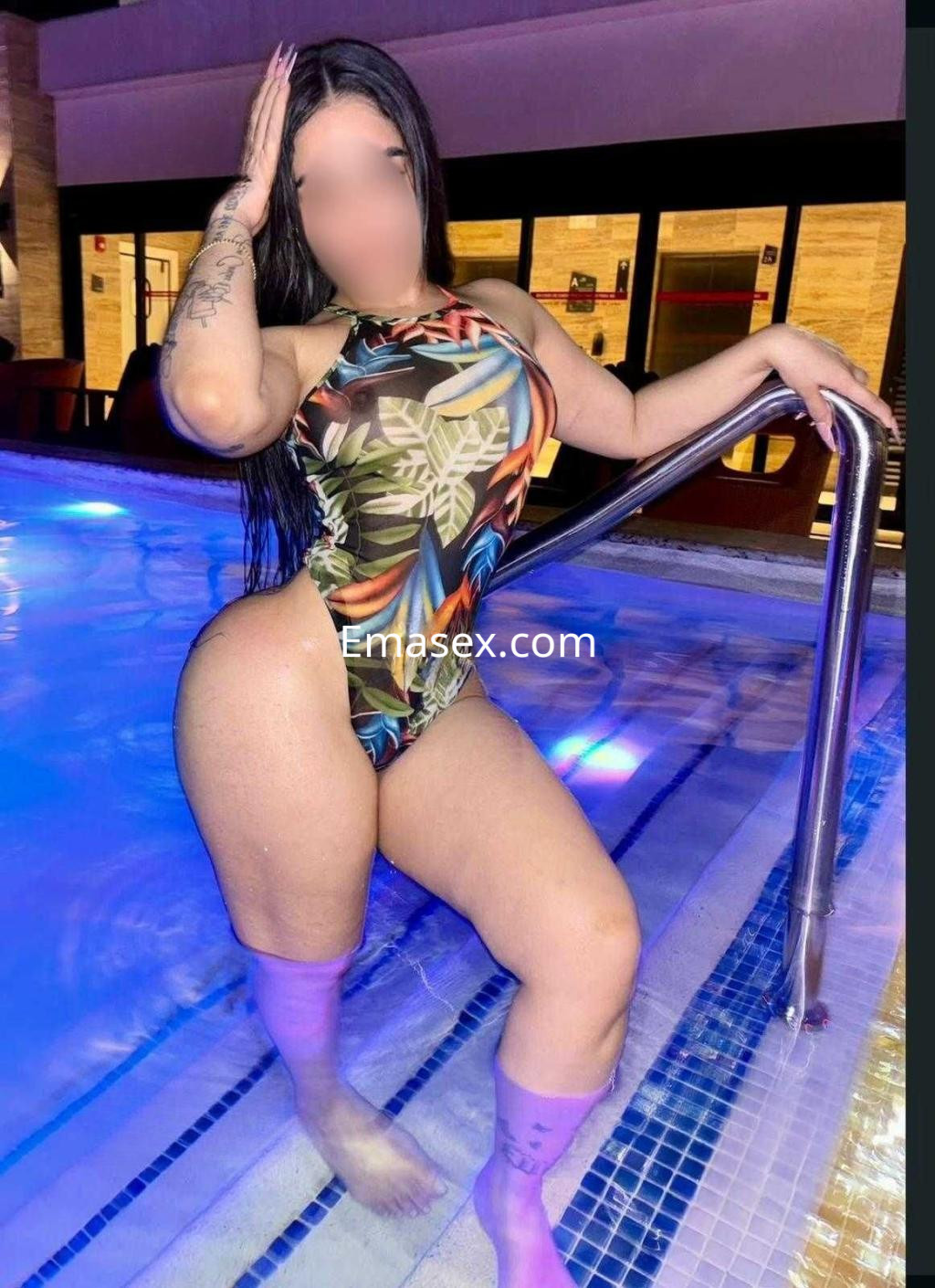 Escort posando en una piscina con un traje de baño colorido y calcetas moradas, en un ambiente relajante en Madrid.