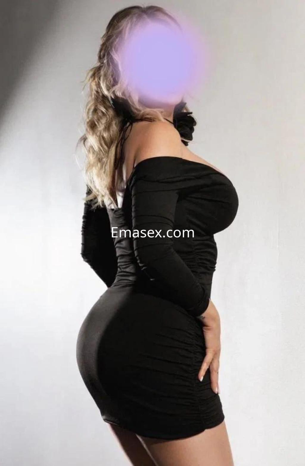 Escort en Madrid con vestido negro ajustado que resalta su figura, posando de perfil con cabello ondulado.