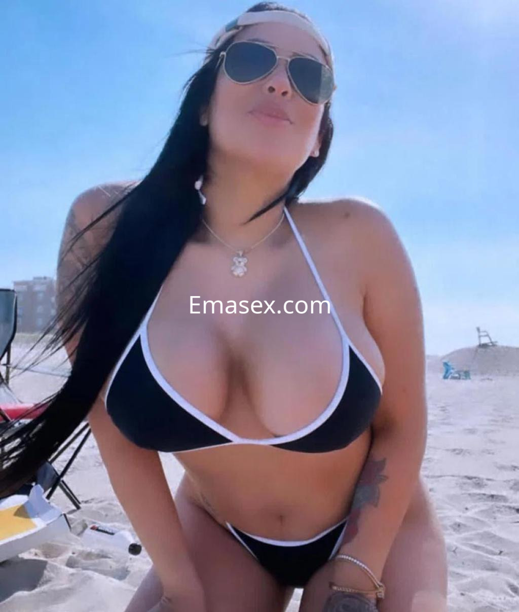 Puta posando en la playa de Pontevedra, con un bikini negro y gafas de sol, mostrando una actitud seductora.
