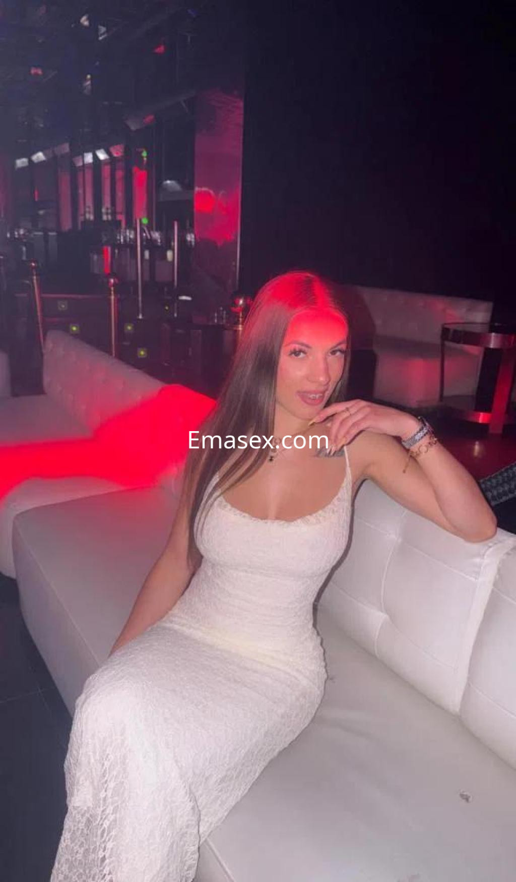 Puta en Tenerife, sentada en un sofá blanco, luciendo un vestido largo y ajustado de color blanco.