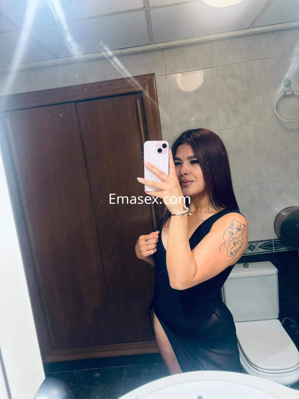 Escort en Sevilla, con cabello largo y lacio, viste un vestido negro semitransparente y muestra un tatuaje en el brazo.