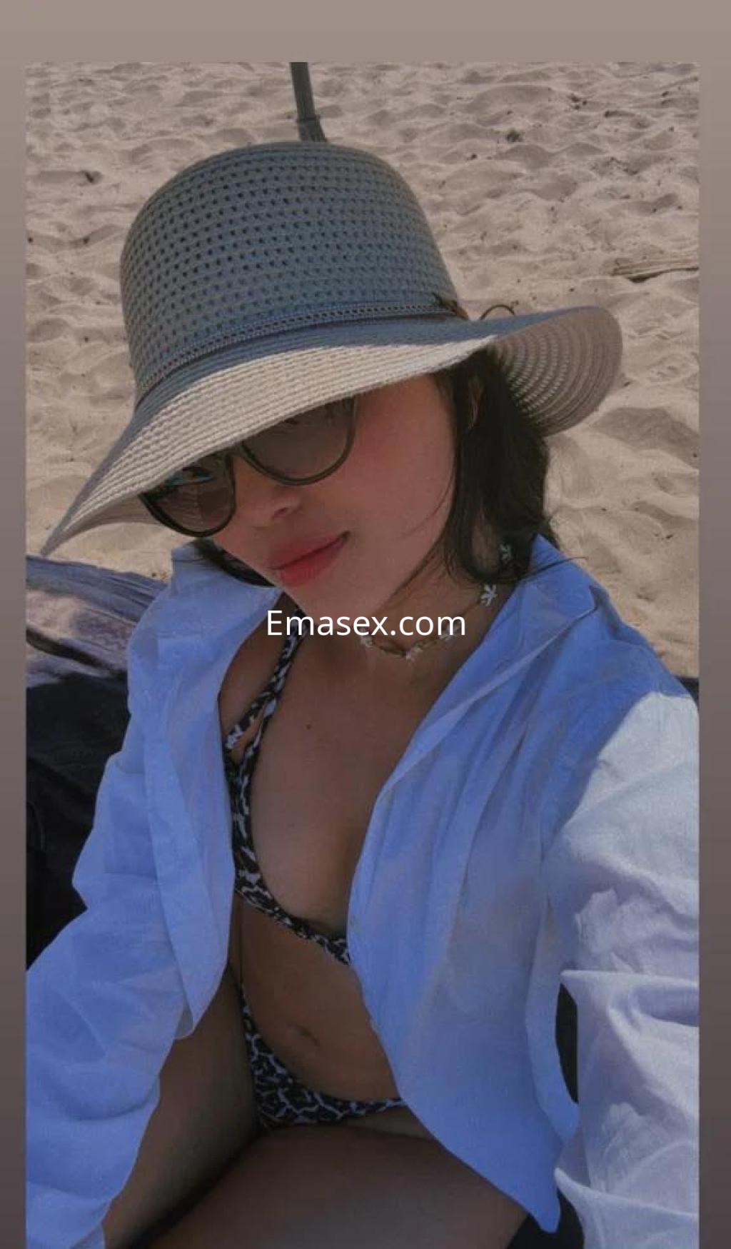 La puta luce un bikini de estampado animal y una camisa blanca, disfrutando del sol en la playa de Valencia.