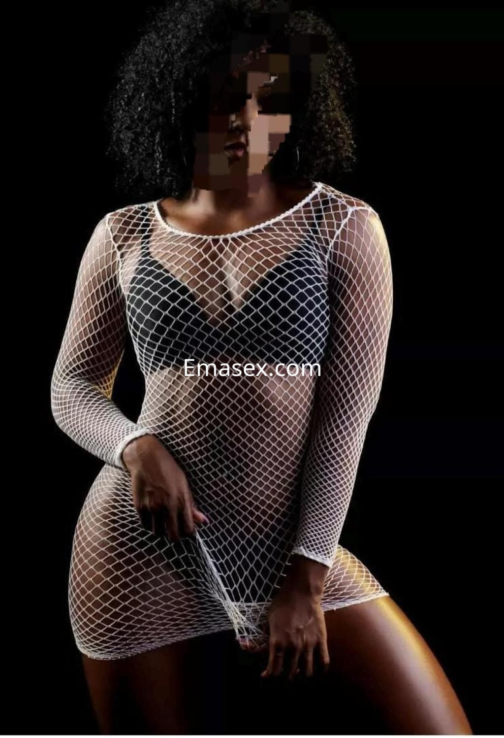 Puta en Coruña, luciendo un vestido de malla blanca con mangas largas, en un fondo oscuro y con una pose seductora.