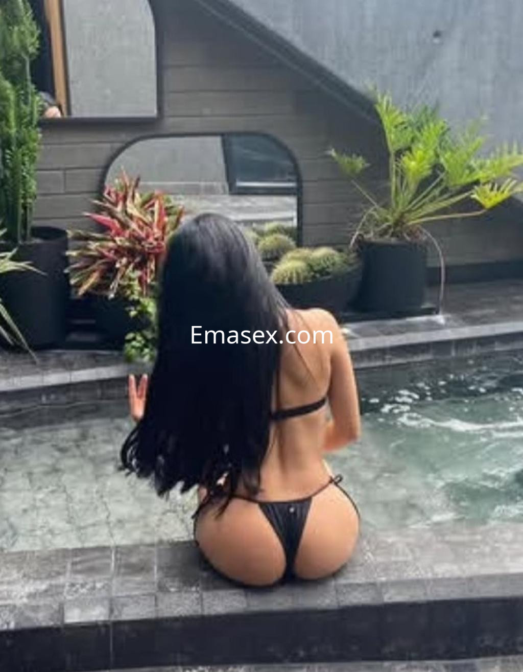 La puta está sentada en el borde de una piscina, luciendo un bikini negro y con el pelo largo y lacio en Pamplona.