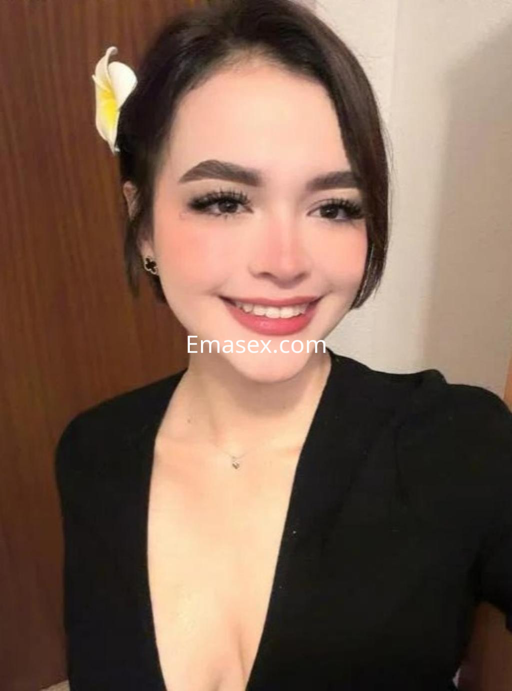 Puta con cabello oscuro y corto, sonriente, lleva un vestido negro y una flor en la cabeza, en Valencia.