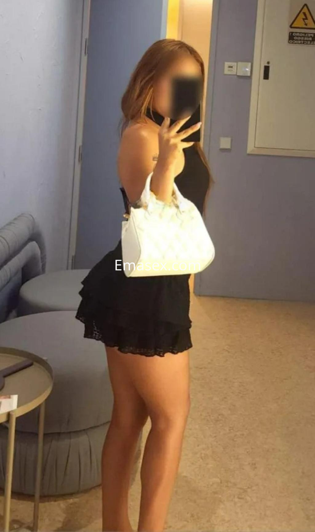 La puta en Valencia posa de perfil con un vestido negro corto y una bolsa blanca, mostrando su figura.