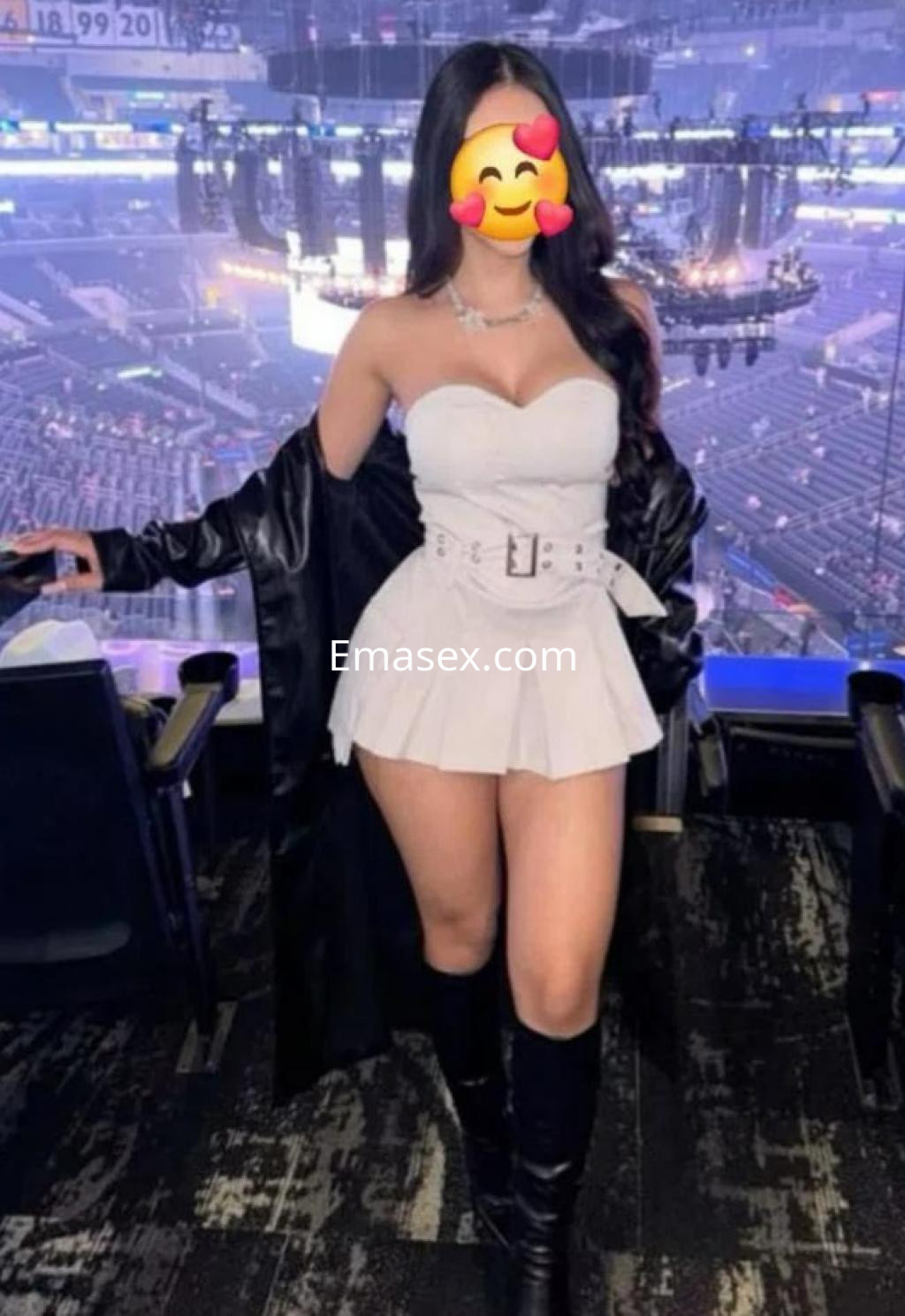 Escort en Toledo luce un vestido blanco ajustado con cinturón y botas altas, posando en un estadio.