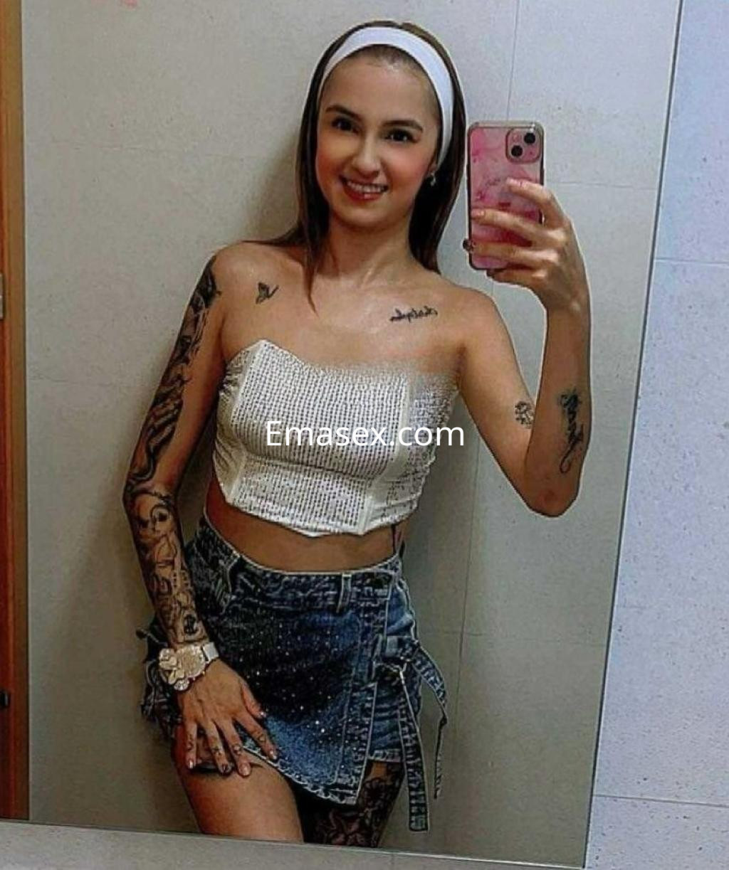 Puta en Toledo, luciendo un top blanco sin mangas y una falda de mezclilla, con tatuajes visibles y un peinado con diadema.