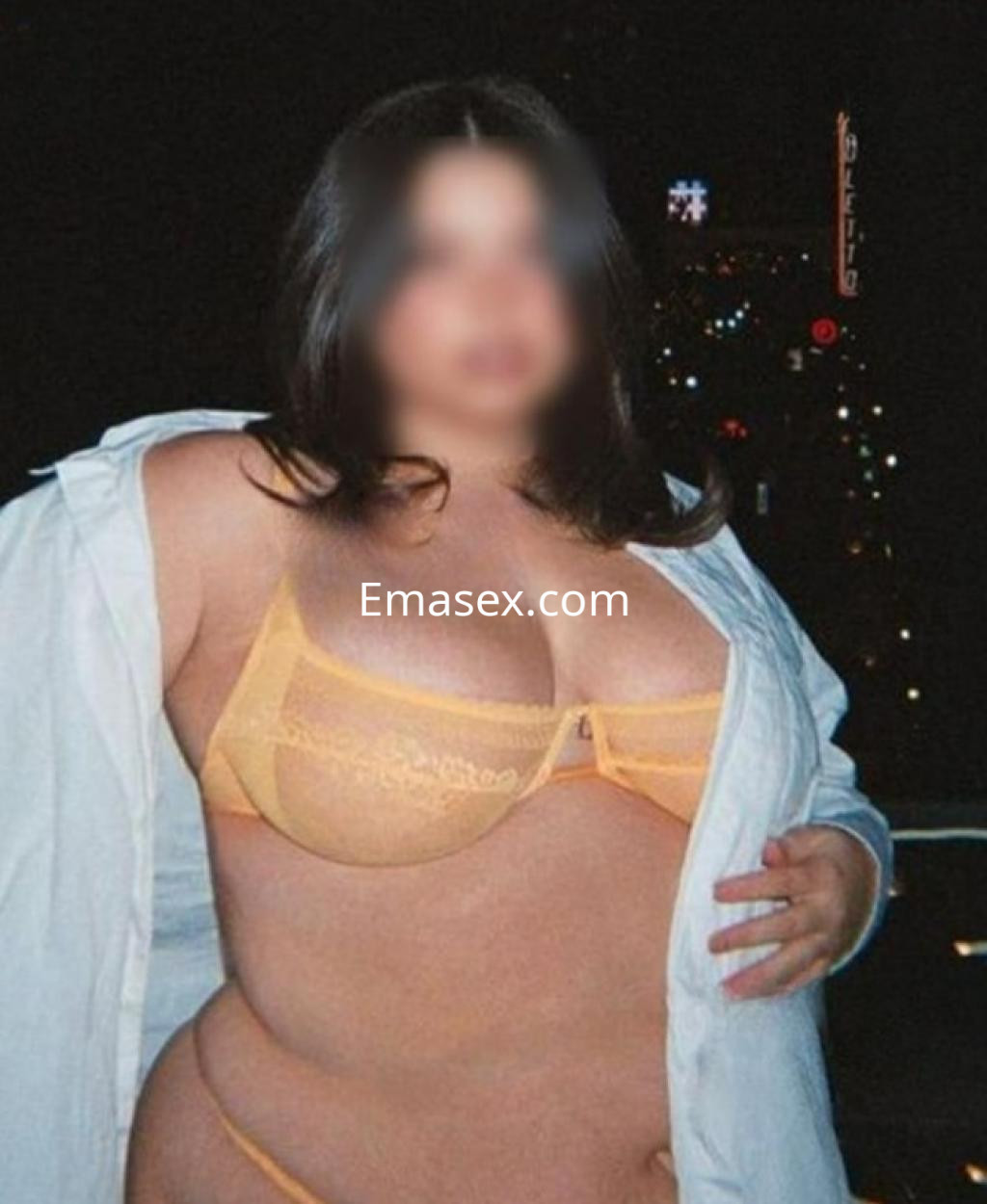 Escort en Castellón con cabello oscuro, usando un sujetador amarillo y una camisa blanca abierta sobre un fondo nocturno.