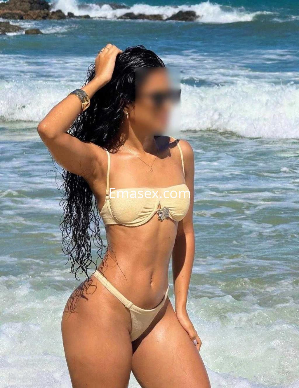Escort en Alicante con cabello largo y ondulado, luciendo un bikini claro frente al mar.
